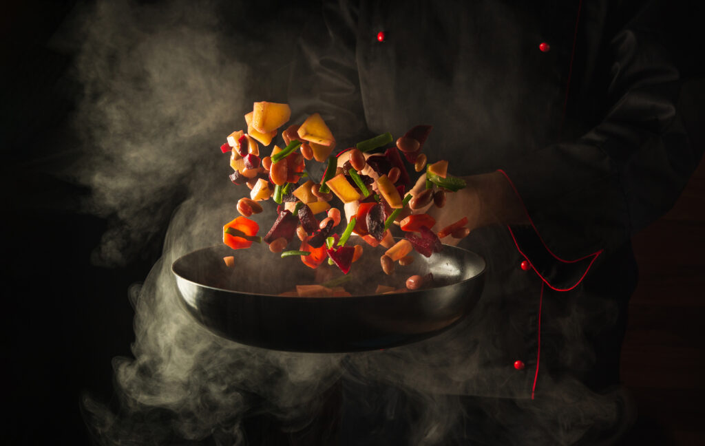 Chef prepares food in a hot pan with steam on a black background. The concept of restaurant and hotel service. Haute cuisine or Grande cuisine.