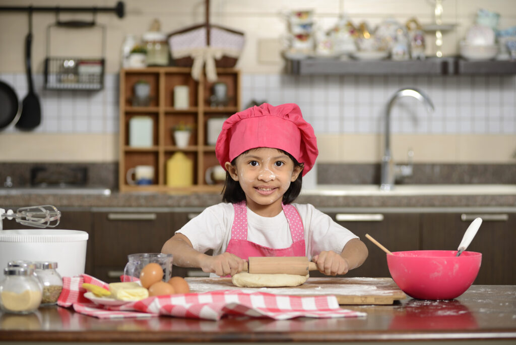 Little asian girl making dough in the kitchen